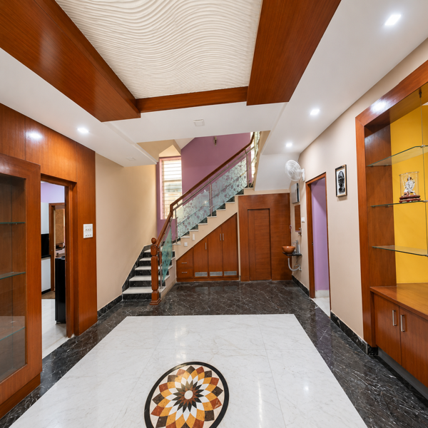 grand entrance foyer, luxury home interior, elegant foyer design, spacious hallway, residential entrance, modern lobby area, marble foyer, white marble flooring, black marble border, decorative floor medallion, inlay flooring, staircase interior, glass staircase railing, wooden handrail, floating staircase, under stair storage, built in cabinets, wooden wall paneling, custom woodwork, display cabinet, glass display shelves, decorative shelving, interior showcase, recessed lighting, false ceiling, wooden ceiling accents, textured ceiling design, warm interior decor, neutral wall colors, accent wall, home entrance design, architectural interior, premium residence, upscale home, family residence, duplex interior, multi level home, staircase landing, hallway storage, wall mounted fan, utility wash area, spacious living area, furnished home, student accommodation, students, business professionals, working professionals, executive accommodation, rental property, urban housing, comfortable living space, move in ready home.